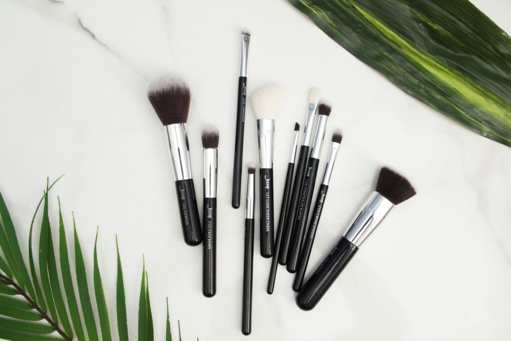 Flat lay of various makeup brushes on a marble surface with green leaves.